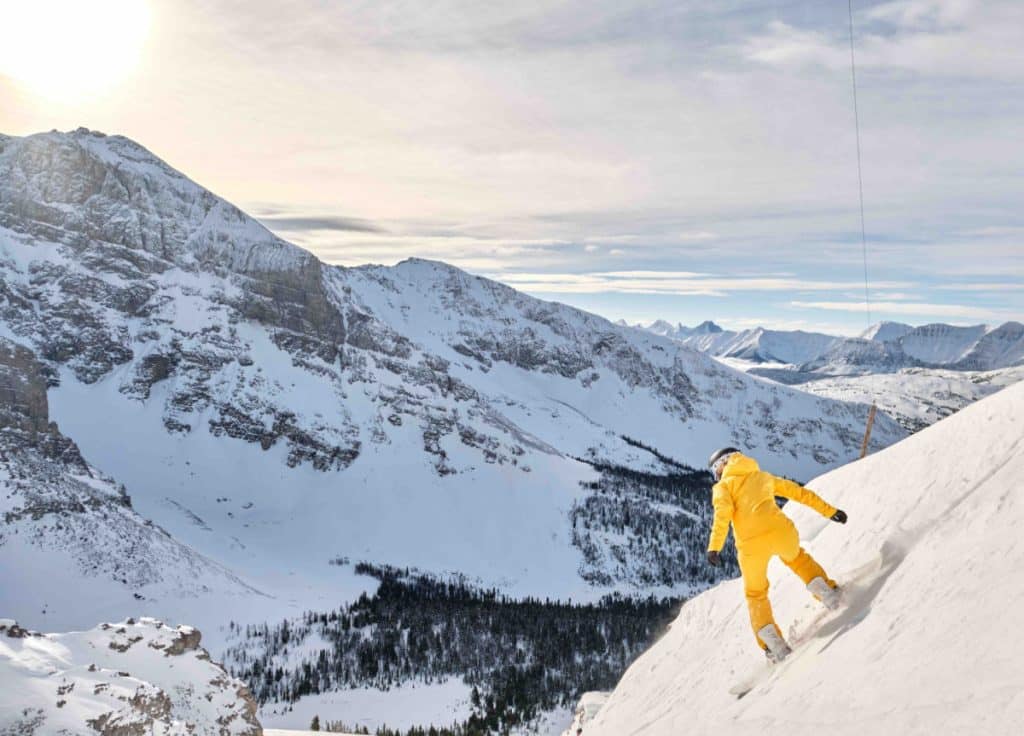 woman in yellow snowsuit snowboarding